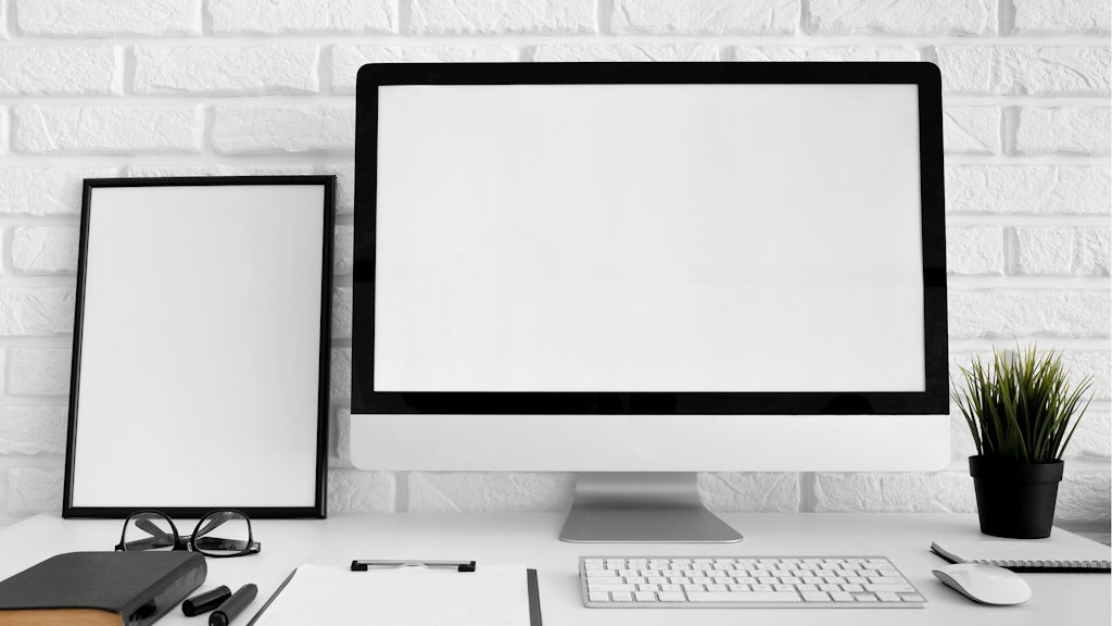 Zu sehen ist ein Arbeitsplatz mit Klemmbrett, Tastatur und Maus sowie mit einem grossen Bildschirm.